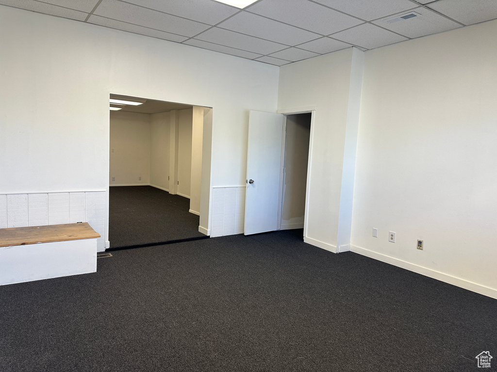 Empty room featuring a paneled ceiling and dark colored carpet