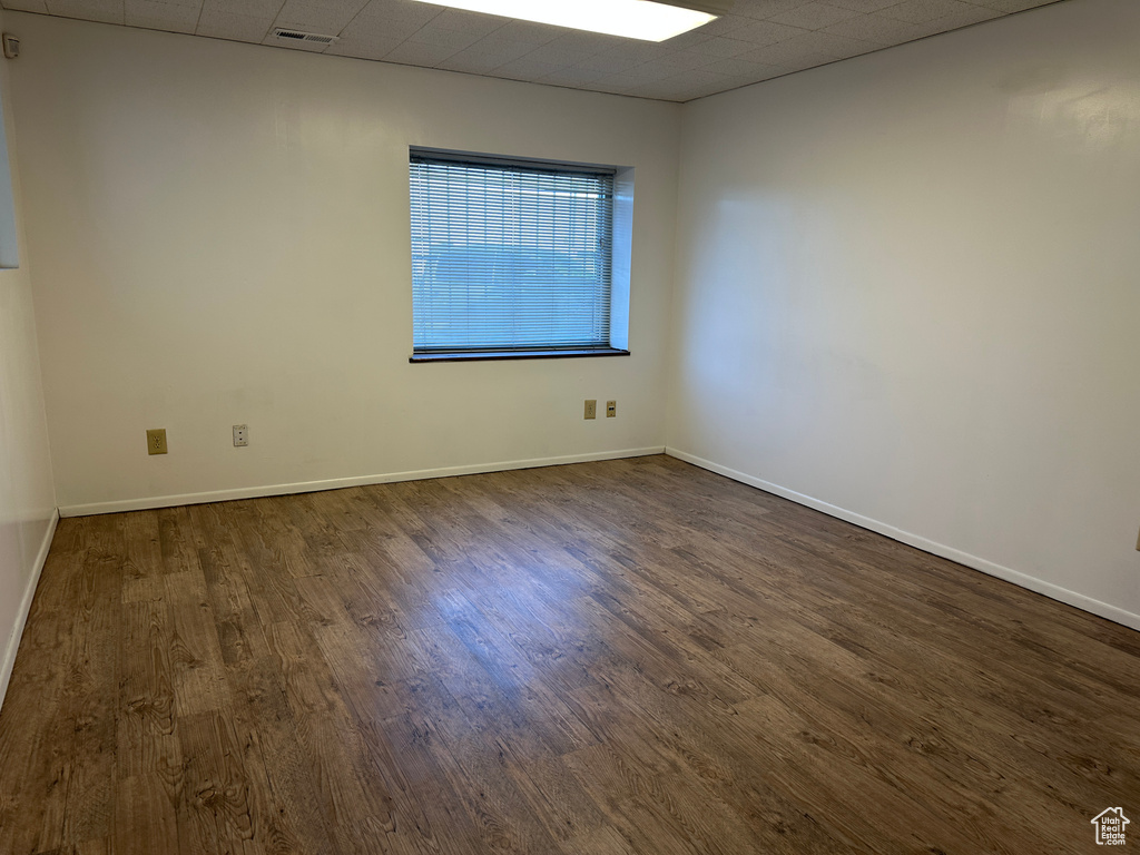 Empty room featuring a drop ceiling and dark hardwood / wood-style floors