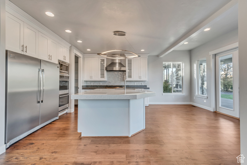 Kitchen with stainless steel appliances, light hardwood / wood-style floors, pendant lighting, wall chimney range hood, and white cabinetry