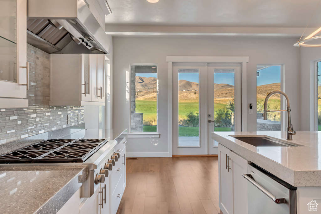 Kitchen with appliances with stainless steel finishes, wall chimney exhaust hood, white cabinetry, and sink