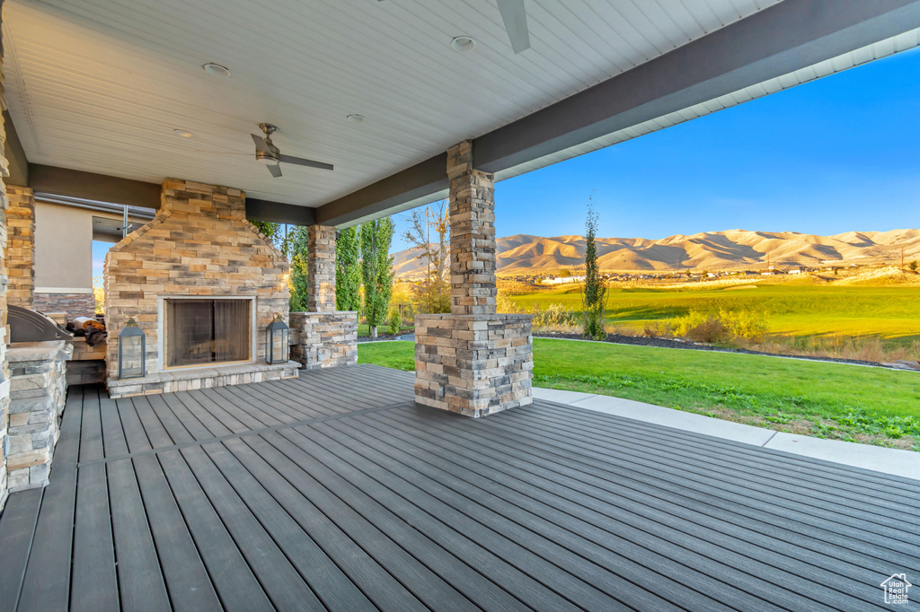 Deck featuring a lawn, an outdoor stone fireplace, a mountain view, and ceiling fan