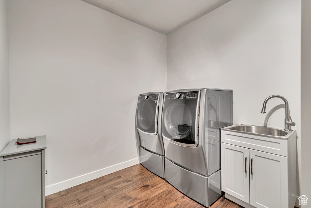 Clothes washing area featuring dark wood-type flooring, washing machine and clothes dryer, cabinets, and sink