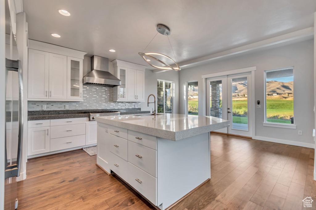 Kitchen with wall chimney exhaust hood, pendant lighting, a center island with sink, dark hardwood / wood-style floors, and white cabinetry