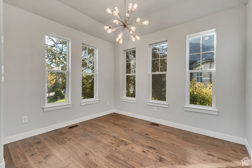 Empty room featuring wood-type flooring and a notable chandelier