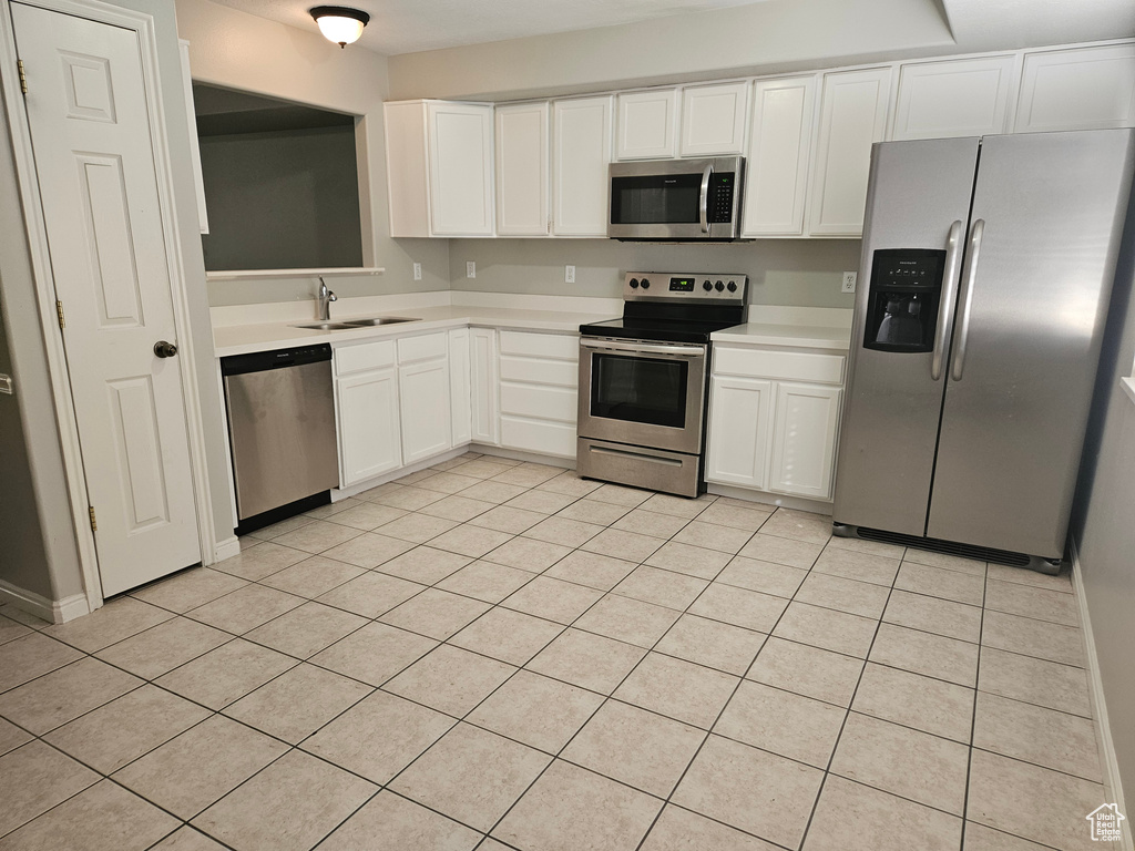 Kitchen featuring white cabinets, light tile patterned flooring, appliances with stainless steel finishes, and sink