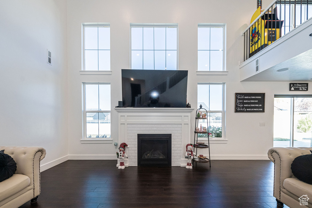 Living room with a brick fireplace, a high ceiling, and dark hardwood / wood-style flooring