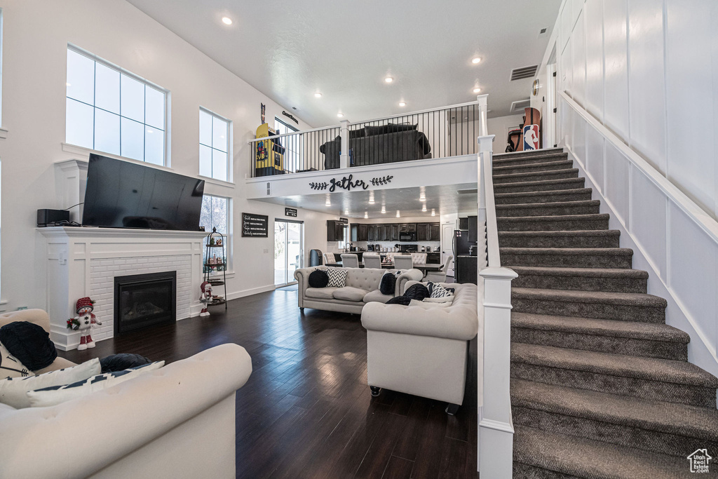 Living room featuring a towering ceiling, dark hardwood / wood-style flooring, and a brick fireplace