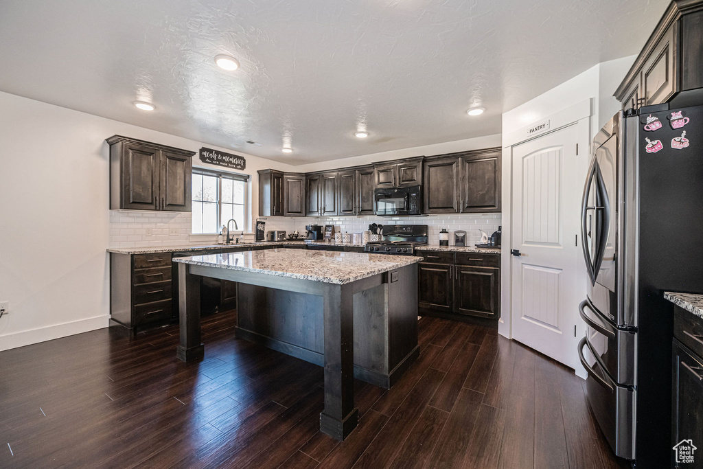 Kitchen with sink, a textured ceiling, black appliances, a center island, and dark hardwood / wood-style flooring