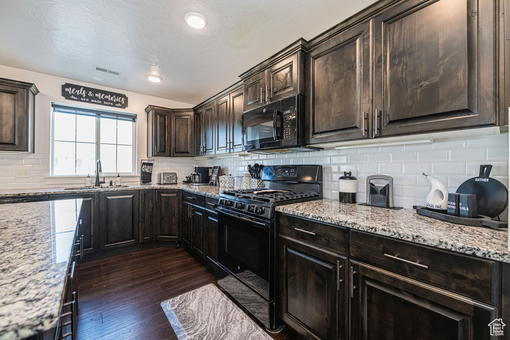 Kitchen with dark wood-type flooring, light stone counters, tasteful backsplash, black appliances, and sink