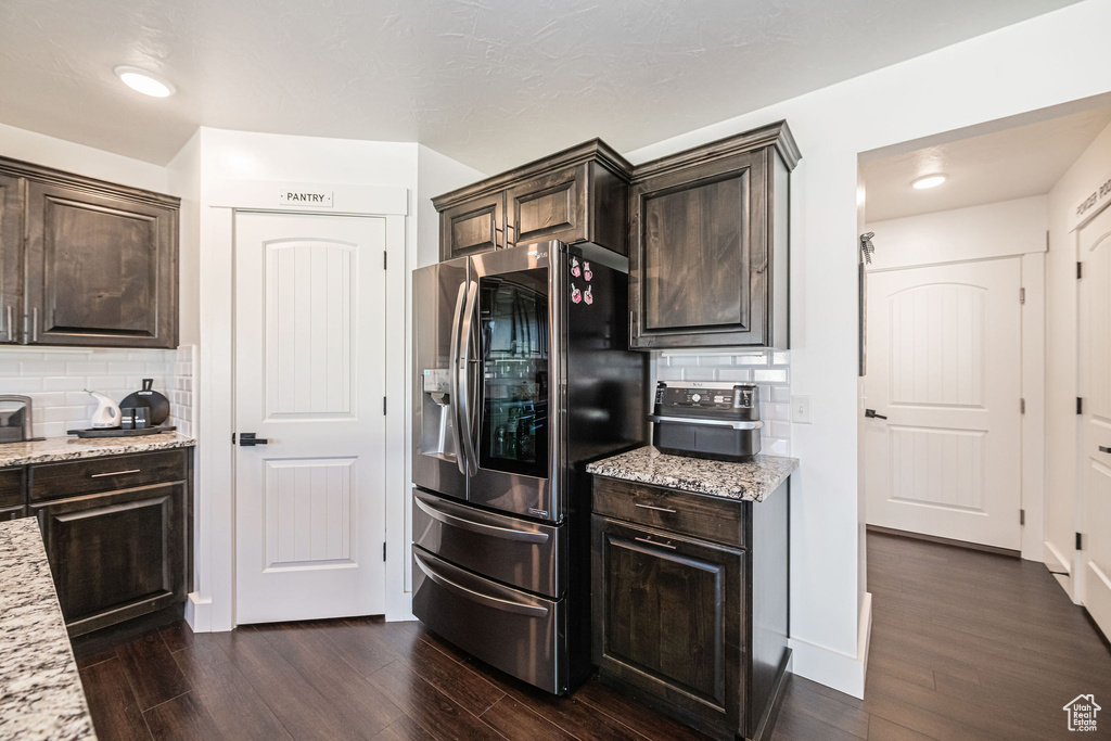 Kitchen featuring stainless steel refrigerator with ice dispenser, light stone countertops, dark wood-type flooring, and tasteful backsplash