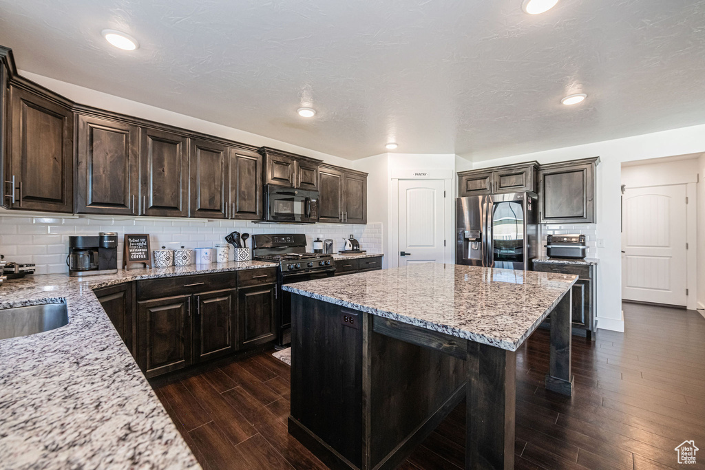 Kitchen featuring black appliances, backsplash, a center island, and dark wood-type flooring