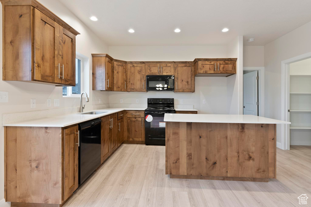 Kitchen featuring black appliances, a kitchen island, sink, and light hardwood / wood-style flooring
