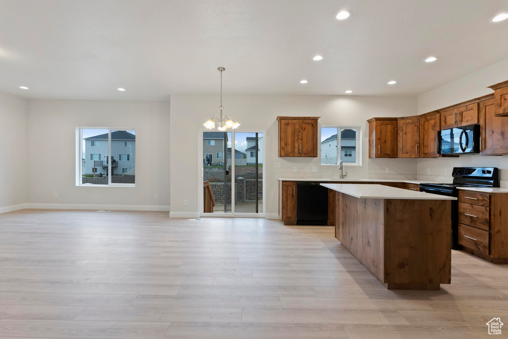 Kitchen with light hardwood / wood-style floors, a center island, an inviting chandelier, black appliances, and decorative light fixtures