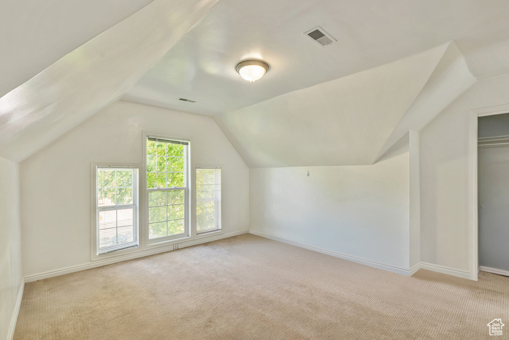 Bonus room with light colored carpet and vaulted ceiling