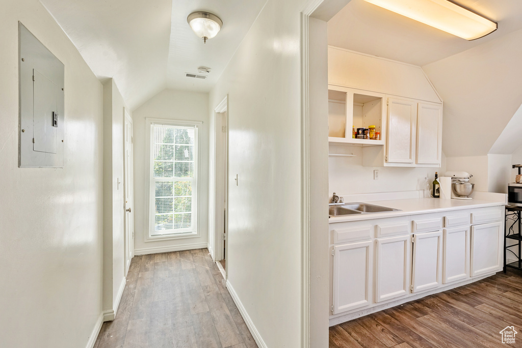 Kitchen featuring light wood-type flooring, electric panel, sink, lofted ceiling, and white cabinetry