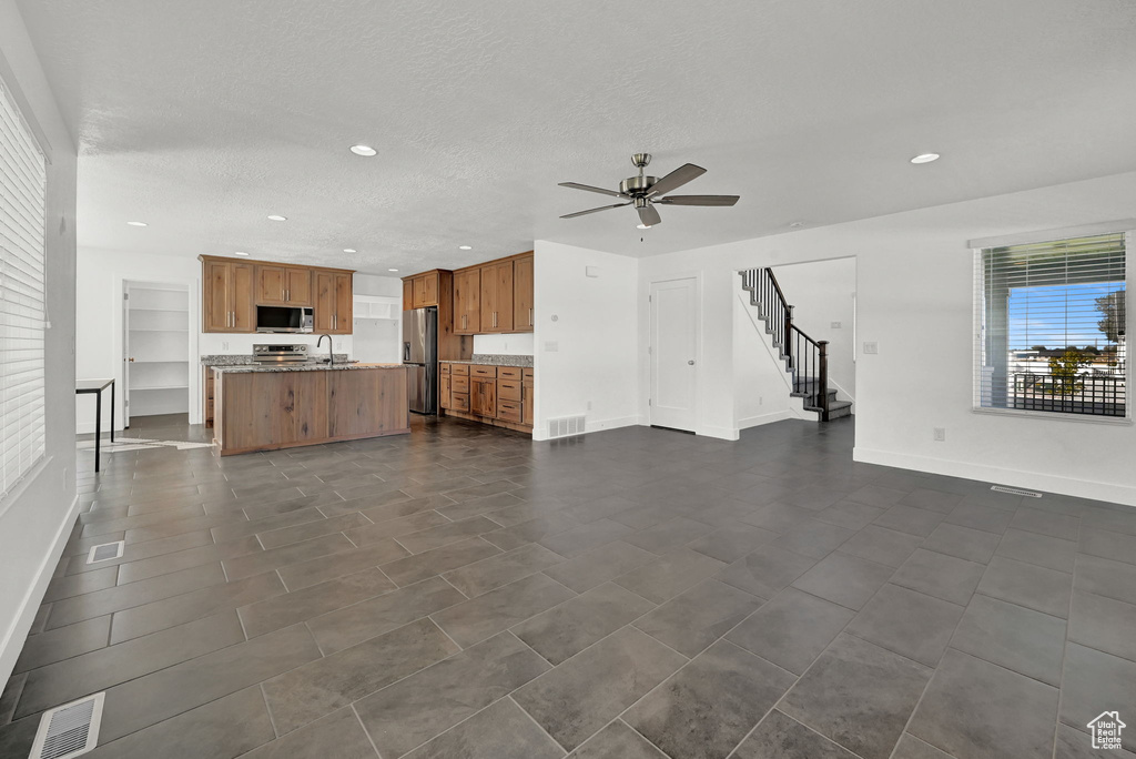 Unfurnished living room featuring ceiling fan, sink, and a textured ceiling