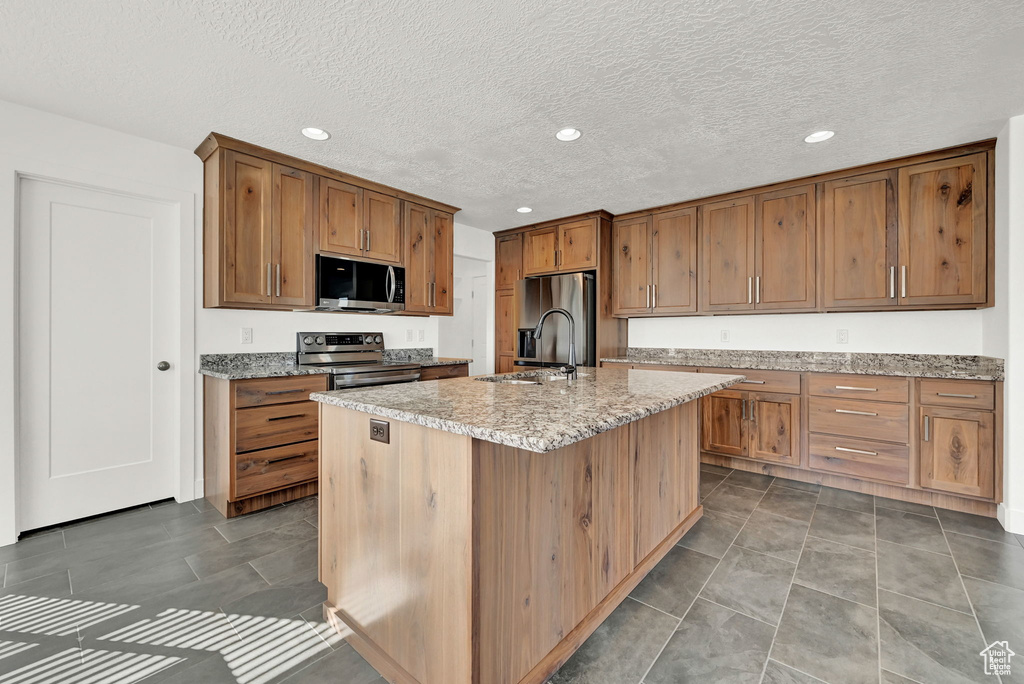 Kitchen featuring a textured ceiling, a kitchen island with sink, sink, and stainless steel appliances