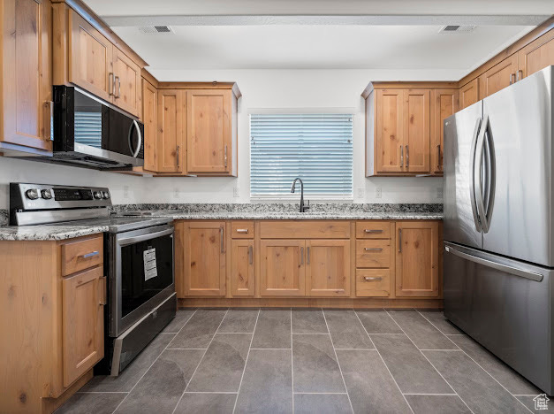 Kitchen with light stone countertops, dark tile patterned flooring, appliances with stainless steel finishes, and sink