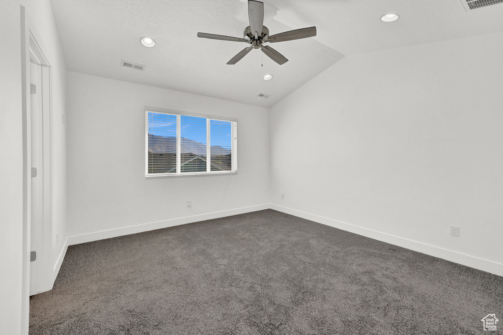 Spare room featuring dark carpet, vaulted ceiling, and ceiling fan