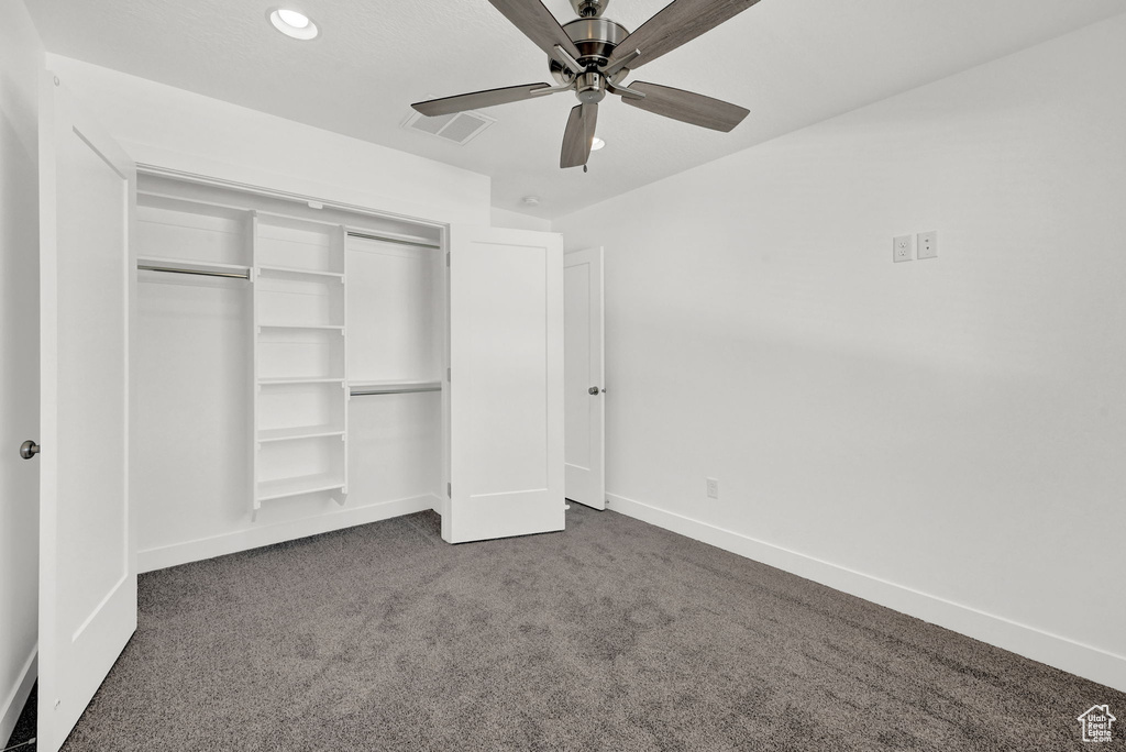 Unfurnished bedroom featuring a closet, dark colored carpet, and ceiling fan