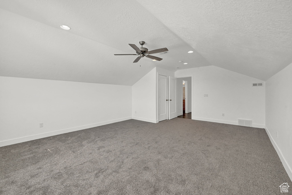 Additional living space featuring dark colored carpet, vaulted ceiling, a textured ceiling, and ceiling fan