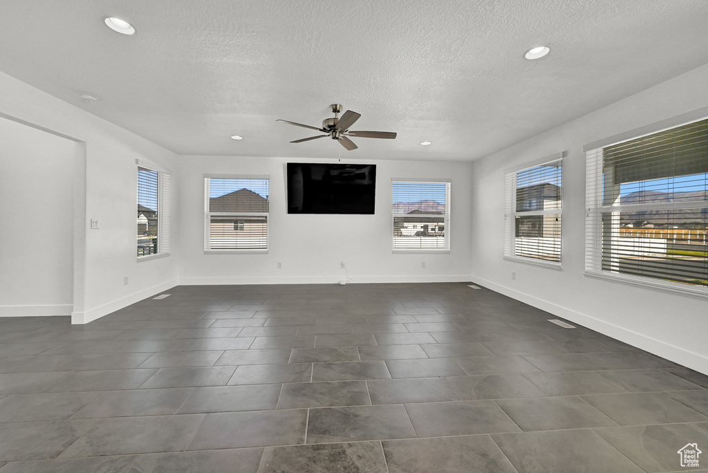 Interior space with ceiling fan, a textured ceiling, dark tile patterned flooring, and a healthy amount of sunlight