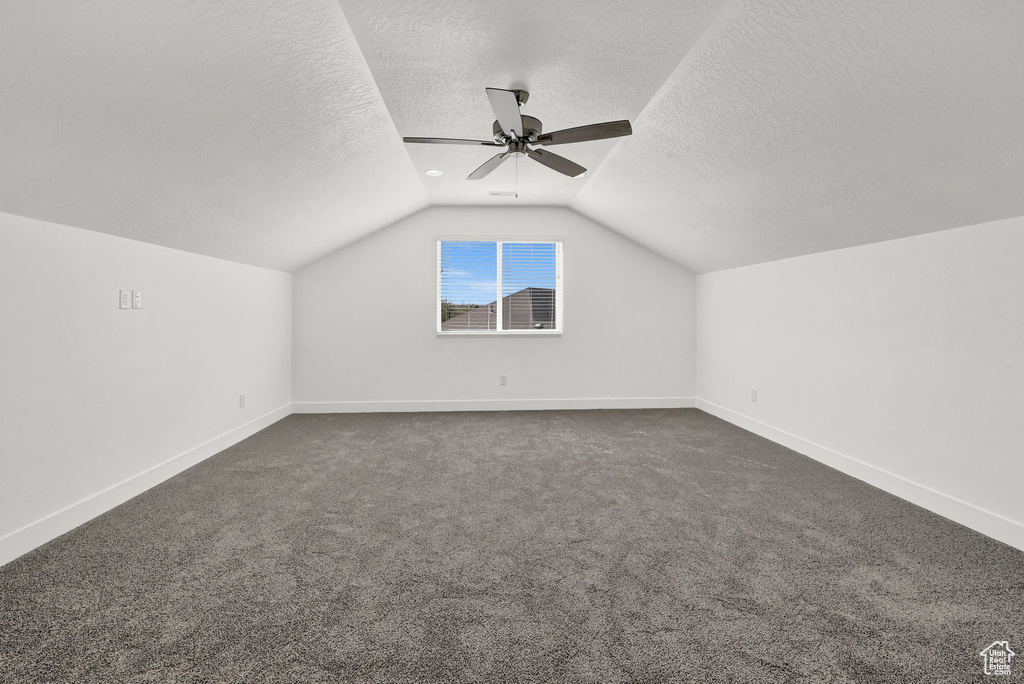 Additional living space featuring a textured ceiling, lofted ceiling, and dark carpet