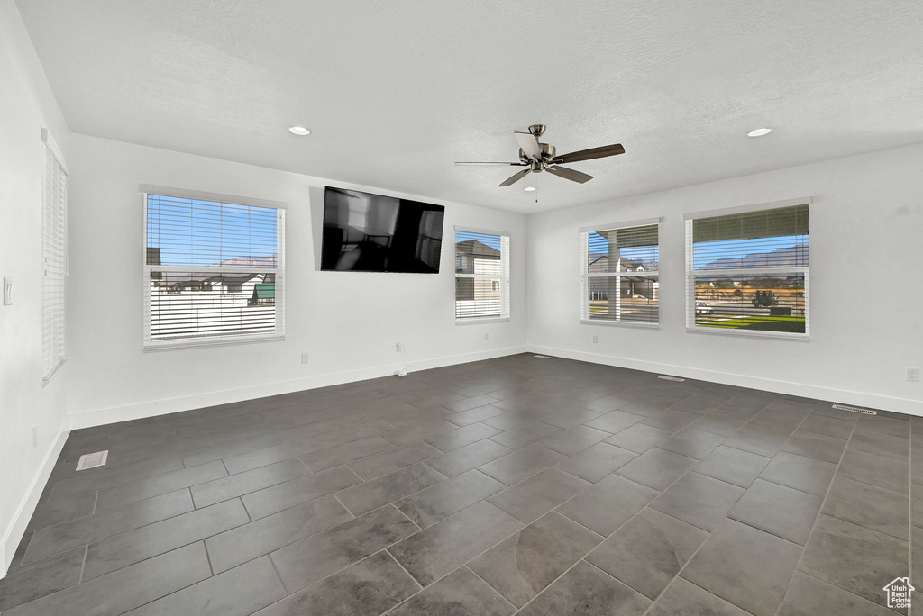 Empty room with ceiling fan, a textured ceiling, and dark tile patterned flooring