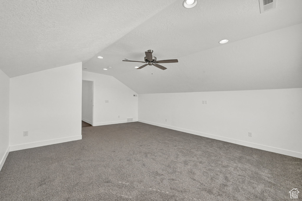 Bonus room featuring dark carpet, lofted ceiling, and a textured ceiling