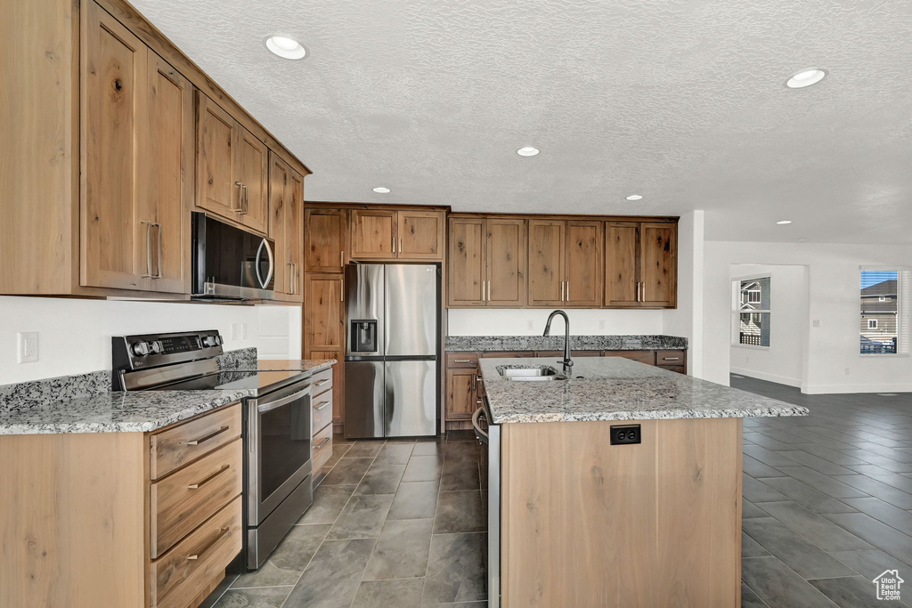 Kitchen featuring light stone counters, sink, a textured ceiling, a kitchen island with sink, and appliances with stainless steel finishes