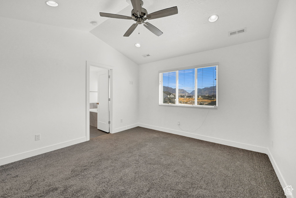 Unfurnished bedroom with dark carpet, lofted ceiling, ceiling fan, and ensuite bath