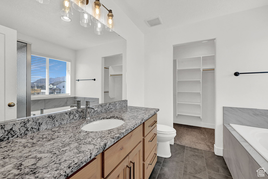 Bathroom with tiled bath, vanity, toilet, and tile patterned floors