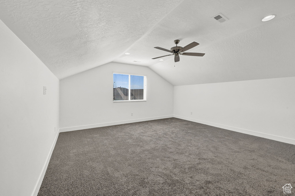 Bonus room with dark carpet, vaulted ceiling, and a textured ceiling