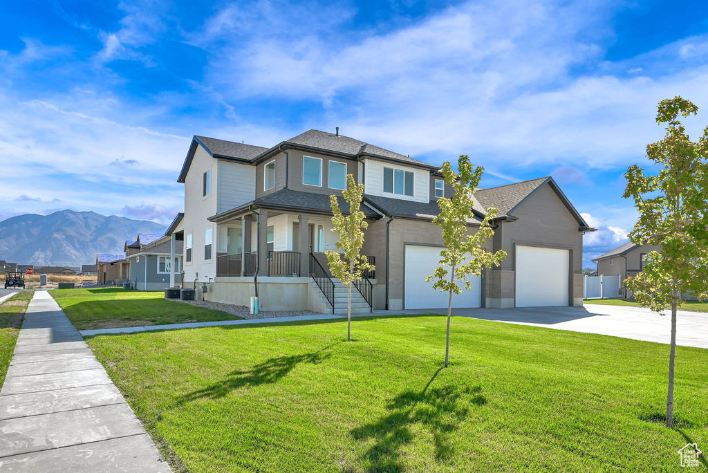 View of front of home featuring a mountain view, covered porch, central AC, a front yard, and a garage