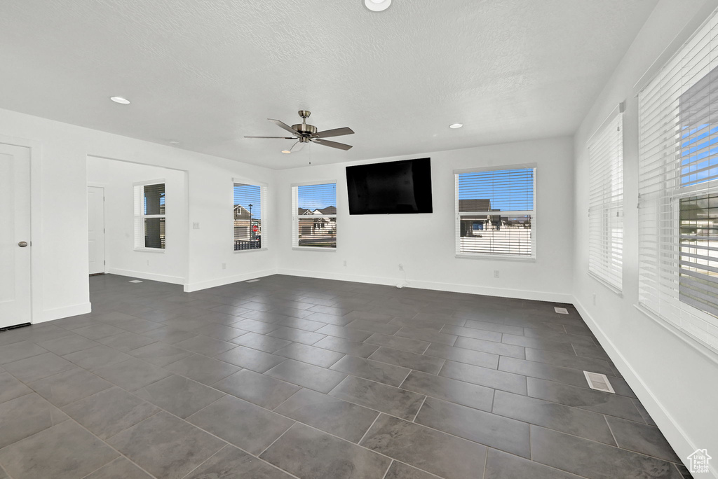 Unfurnished living room featuring ceiling fan, a textured ceiling, and dark tile patterned floors