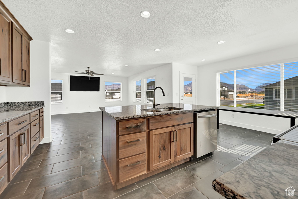 Kitchen featuring light stone counters, ceiling fan, an island with sink, sink, and a textured ceiling