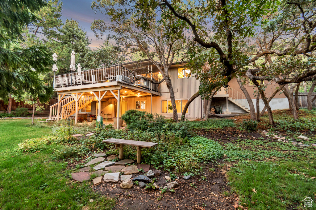 Back house at dusk featuring a wooden deck and a lawn