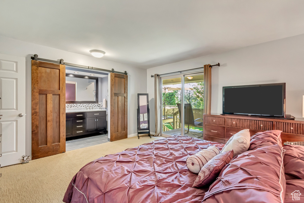 Bedroom with ensuite bath, light colored carpet, access to exterior, and a barn door