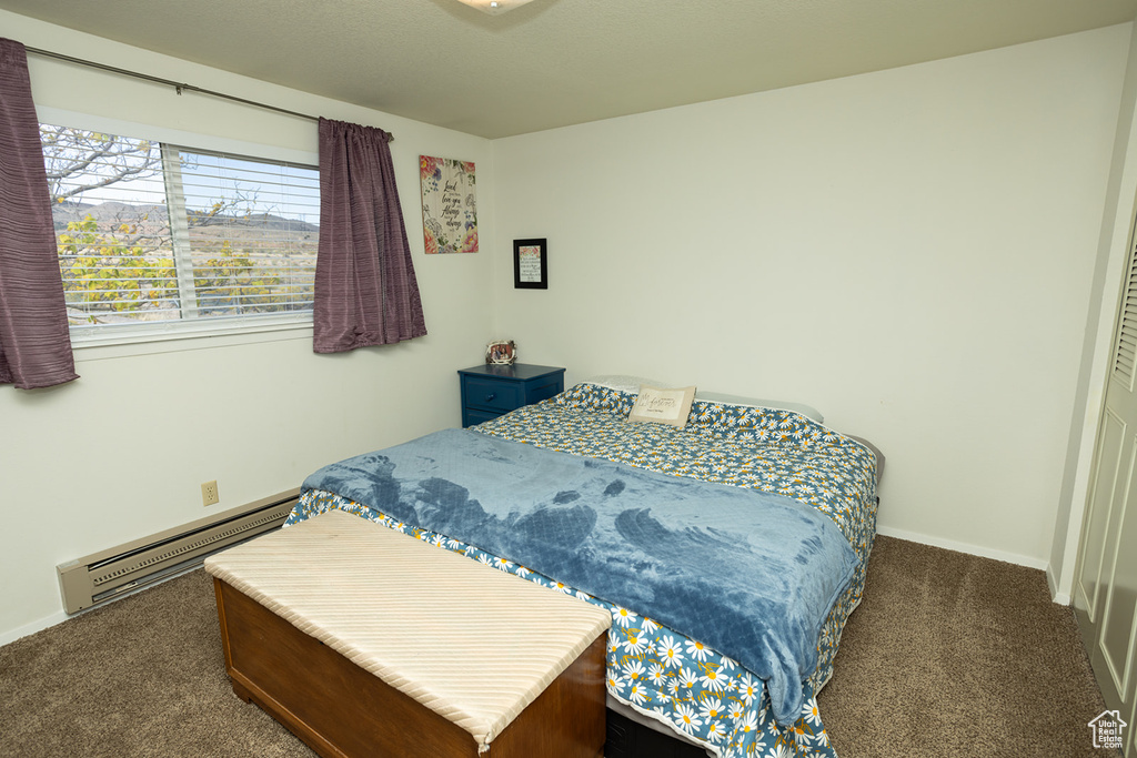 Bedroom with dark colored carpet and a baseboard heating unit