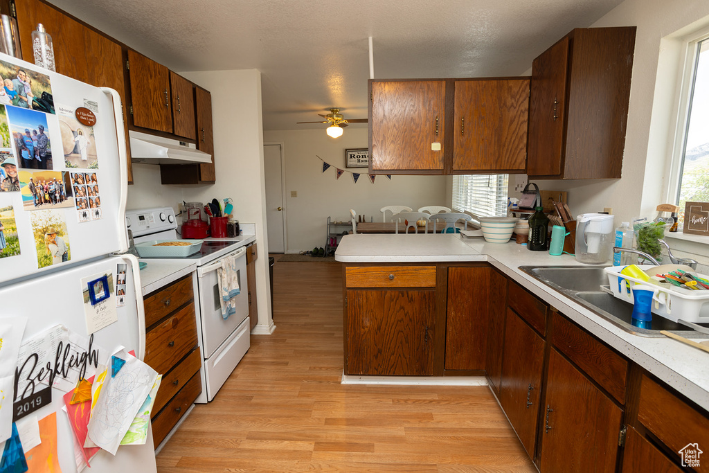 Kitchen with ceiling fan, sink, kitchen peninsula, white appliances, and light wood-type flooring