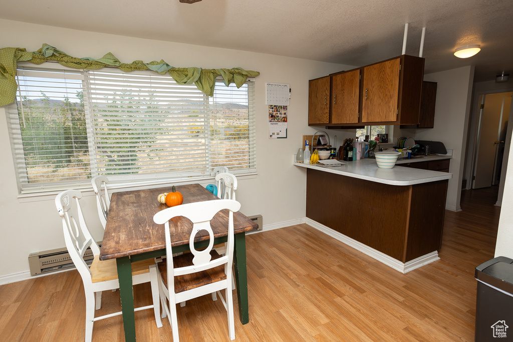 Kitchen with kitchen peninsula, a baseboard radiator, light hardwood / wood-style flooring, and a healthy amount of sunlight