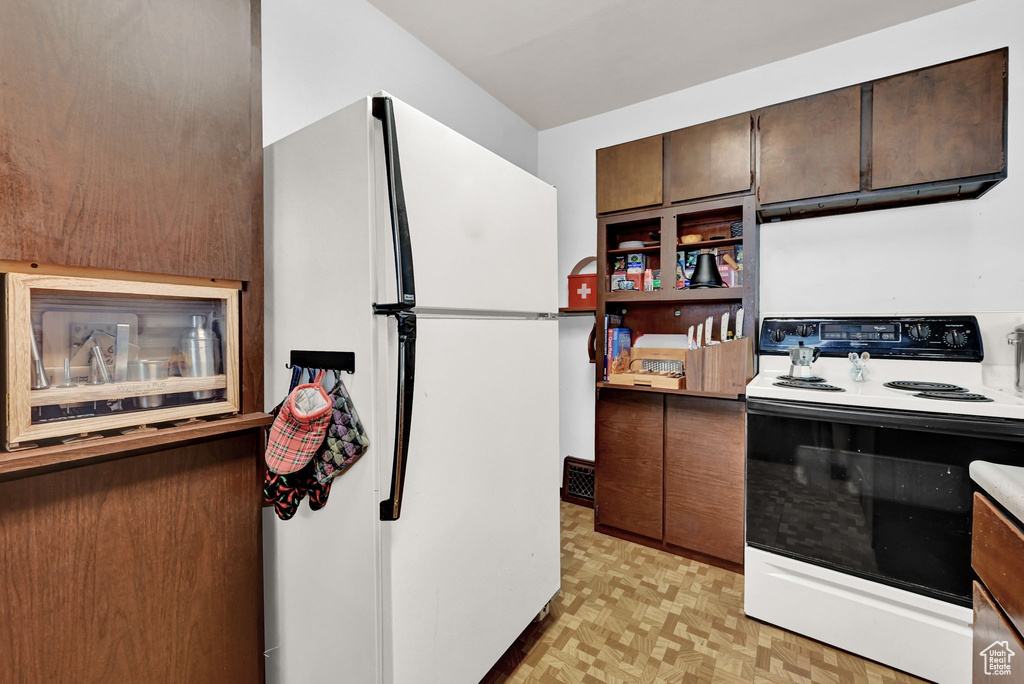 Kitchen featuring white appliances, light parquet floors, and dark brown cabinets