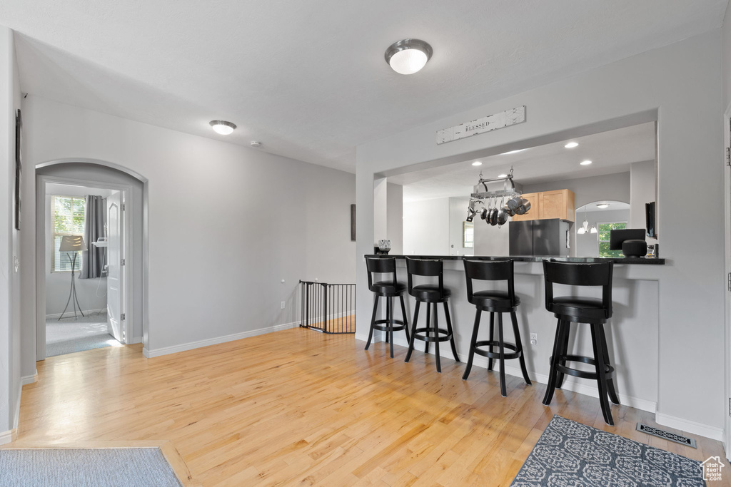 Kitchen featuring light brown cabinetry, a kitchen bar, stainless steel refrigerator, and light hardwood / wood-style flooring