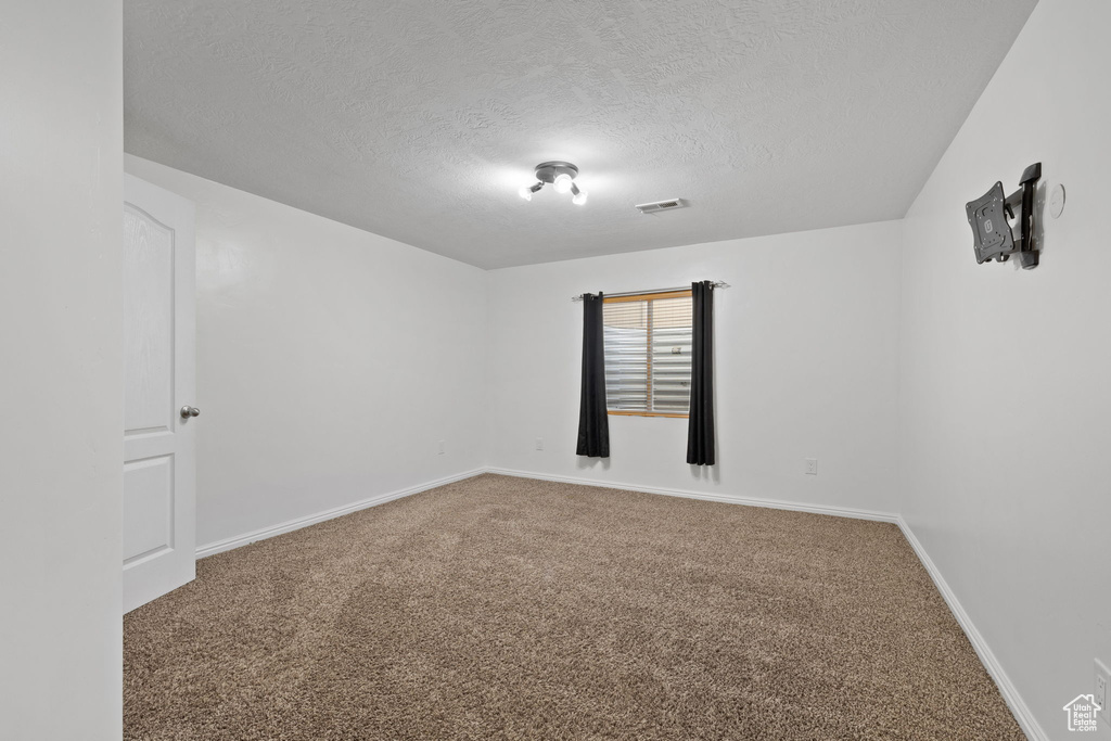 Unfurnished room featuring a textured ceiling and carpet