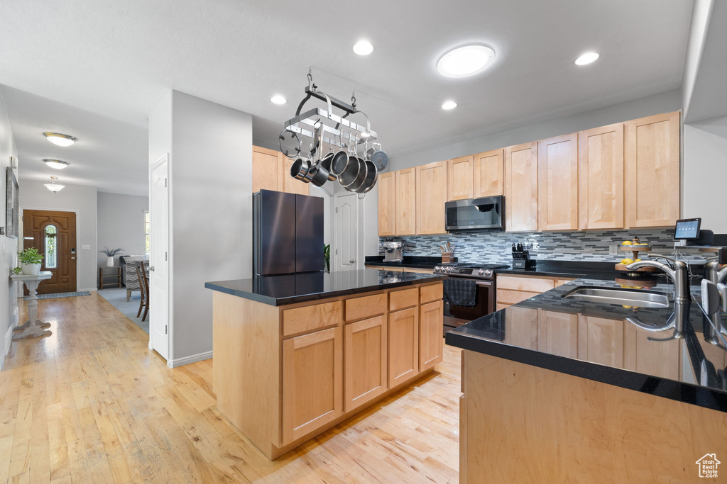 Kitchen with light brown cabinets, stainless steel appliances, light hardwood / wood-style floors, and a center island