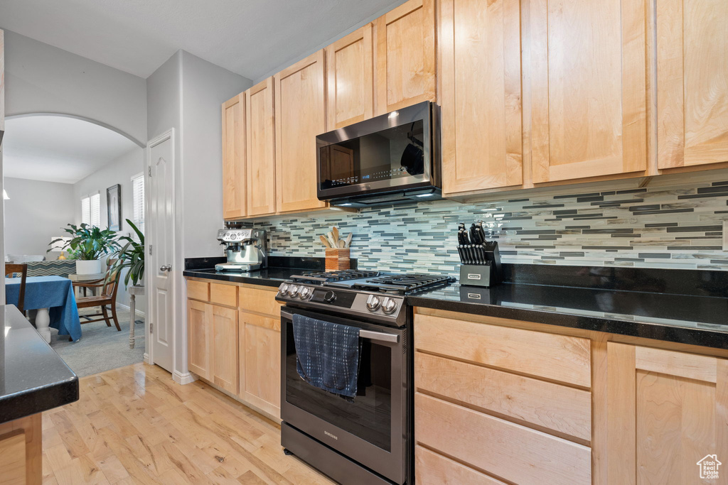 Kitchen featuring appliances with stainless steel finishes, decorative backsplash, light brown cabinets, and light hardwood / wood-style flooring