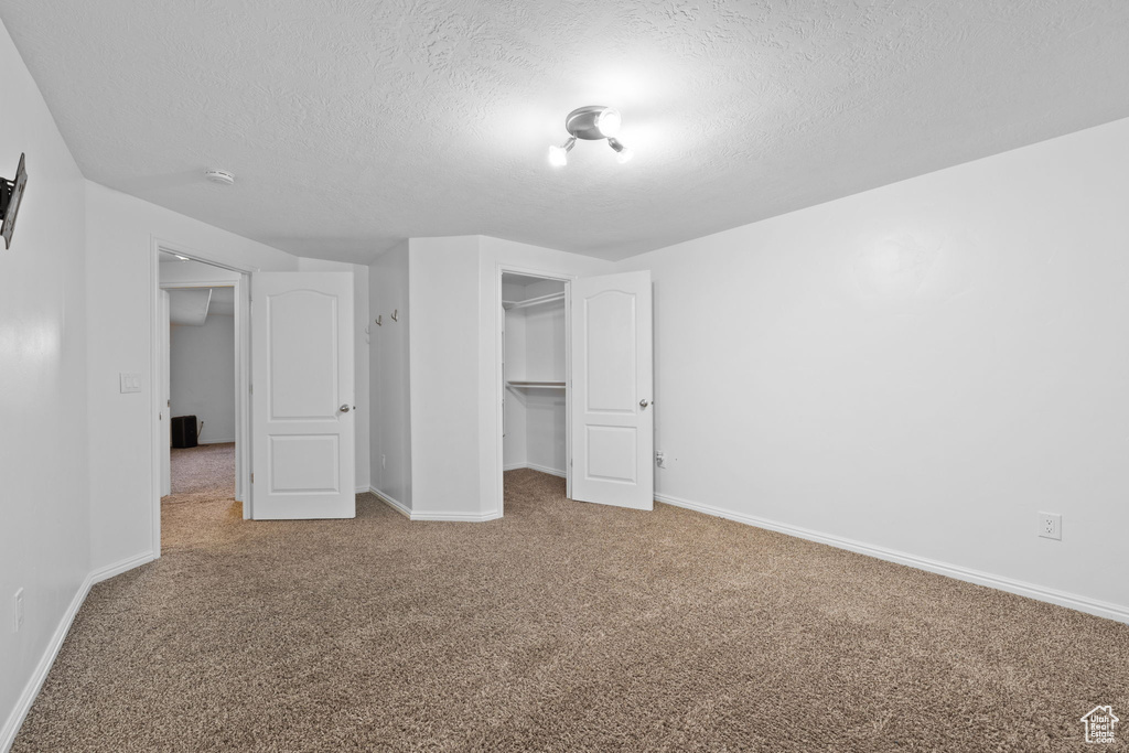 Unfurnished bedroom featuring a closet, a walk in closet, carpet, and a textured ceiling