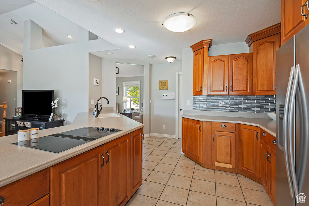 Kitchen with light tile patterned floors, sink, stainless steel refrigerator with ice dispenser, black electric stovetop, and backsplash