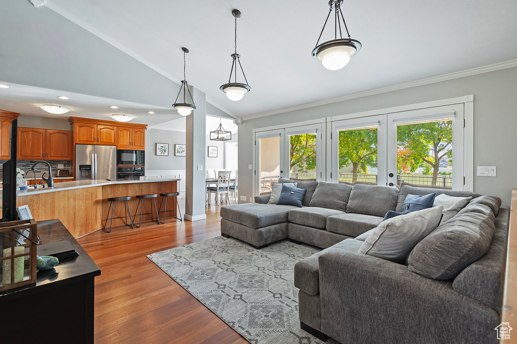 Living room with ornamental molding, a notable chandelier, vaulted ceiling, and light hardwood / wood-style flooring