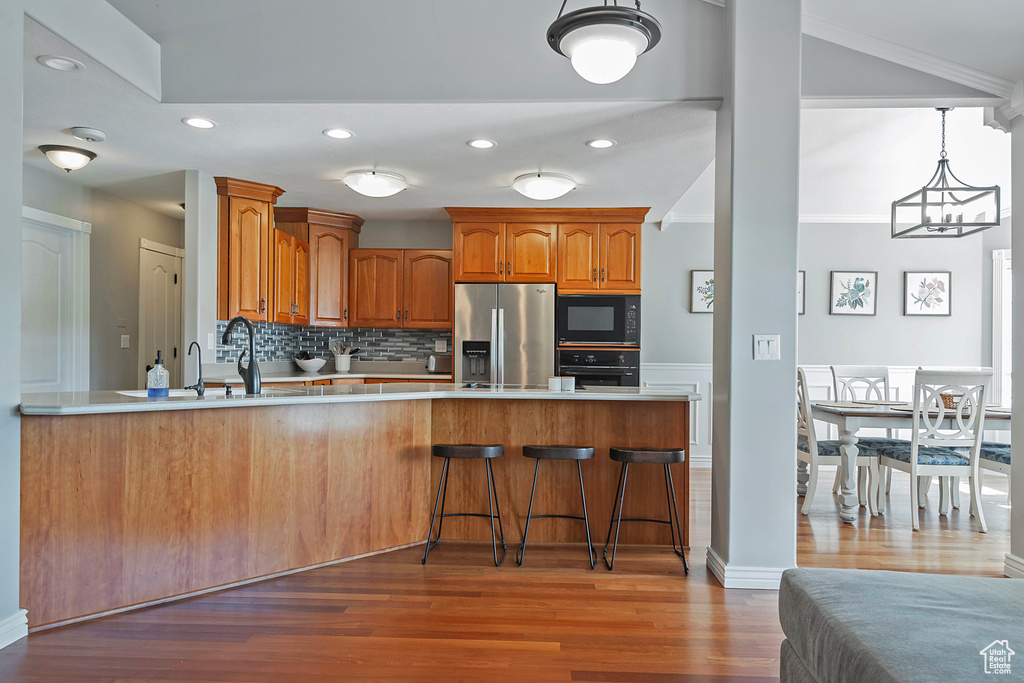 Kitchen with a chandelier, crown molding, hardwood / wood-style floors, kitchen peninsula, and black appliances